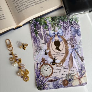 May include: A phone case with a vintage design, featuring lavender flowers, butterflies, bees, and a pocket watch. The case has the text "Lady Whistledown's Society Papers". A gold-coloured keychain with charms and a bee-shaped phone charm are also visible.