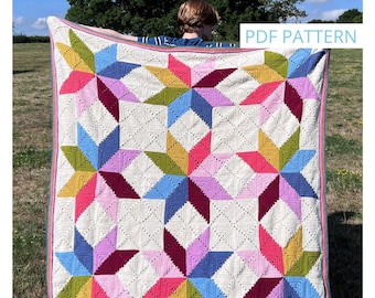 May include: A crochet blanket with a stargazer design in a variety of colors, including pink, blue, green, and yellow. The blanket is being held up by a person in a field. The text "PDF PATTERN" and "Emma Varnam" are visible in the image. The text "Stargazer Crochet Blanket" is visible at the bottom of the image.