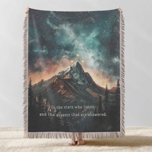 Könnte beinhalten: Eine Decke mit einer Berglandschaft unter einem Sternenhimmel. Das Design zeigt einen Berggipfel mit drei hellen Sternen und dem Text "To the stars who listen- and the dreams that are answered."