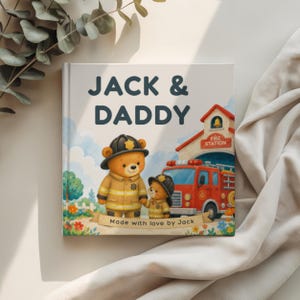 Może przedstawiać: Kwadratowa książka w twardej oprawie zatytułowana JACK & DADDY z ilustracją dw&oacute;ch pluszowych misi&oacute;w w strojach strażackich przed remizą i czerwonym wozem strażackim. Na dole znajduje się baner z napisem Made with love by Jack.