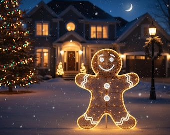 Op de afbeelding: Een verlichte peperkoekenman-decoratie in een besneeuwde tuin 's nachts. De figuur is omrand met warmwitte lichten en heeft een lachend gezicht. Een kerstboom en een huis met verlichte ramen zijn zichtbaar op de achtergrond.