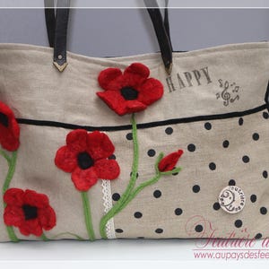 Puede incluir: Bolso tote beige con asas de cuero negro, adornado con amapolas rojas de fieltro y tallos verdes. El bolso presenta lunares negros, la palabra "HAPPY" y un diseño de notas musicales. Un pequeño emblema redondo está en la parte inferior derecha.