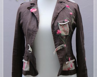 May include: A brown linen jacket with floral embroidery and patchwork details. The jacket has a collar, long sleeves, and a front closure. The jacket is on a white mannequin.