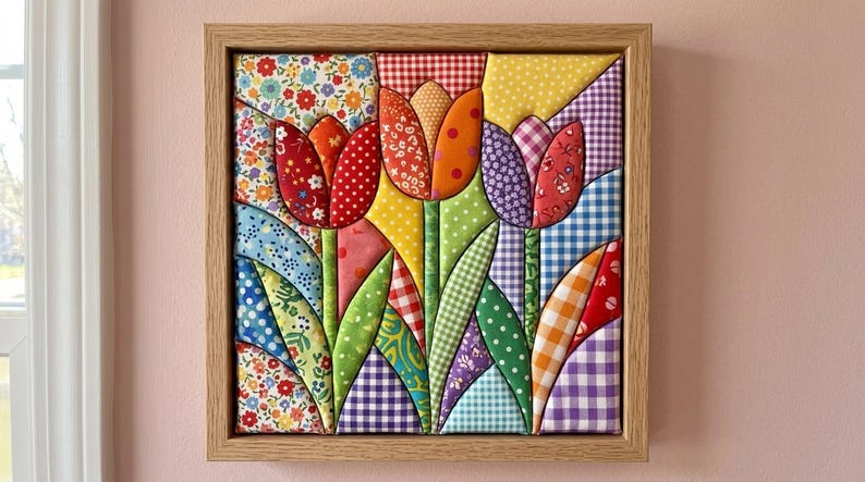 May include: A square fabric wall art piece featuring three quilted tulips in red, orange, and purple, set against a background of various colorful patterned textiles including gingham, floral, and polka dot prints, all encased in a light wood frame.