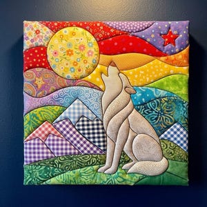Op de afbeelding: Een vierkant stoffen wandkunstwerk met een doorgestikte scène van een beige wolf die naar een grote gele maan met bloemenpatroon huilt. De achtergrond bevat kleurrijke heuvels, paars-wit geblokte bergen en een rode ster in de lucht.