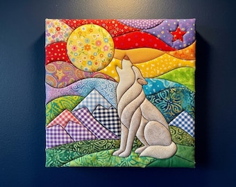 May include: A square fabric wall art piece featuring a quilted scene of a beige wolf howling at a large yellow floral moon. The background includes colourful rolling hills, purple and white gingham mountains, and a red star against a vibrant sky.