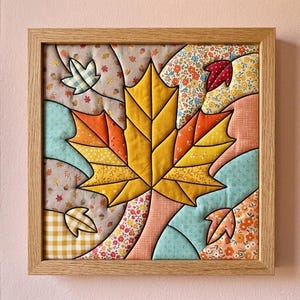 May include: A square wall art piece featuring a central yellow maple leaf surrounded by smaller leaves in a quilted fabric design. The artwork is encased in a light-colored wooden frame and displays various patterns including floral, gingham, and solid colors.