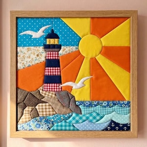 May include: A framed fabric wall art piece featuring a lighthouse with red and white checkered patterns, set against a sunburst of yellow and orange fabric rays. The scene includes white fabric seagulls, rocky terrain, and blue patterned ocean waves.