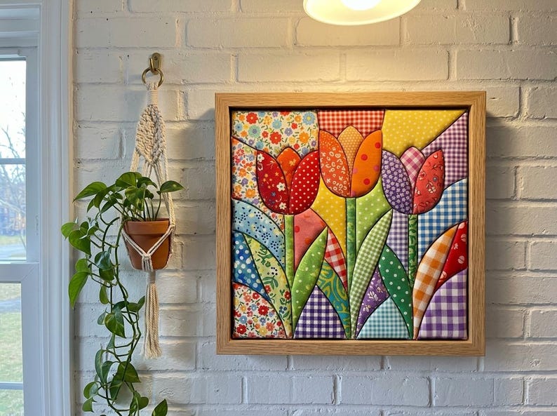 May include: A square fabric wall art piece featuring a quilted tulip design in a light wood frame. The artwork displays three stylized tulips in red, orange, and purple, crafted from various patterned fabrics including gingham, floral, and polka dot prints.