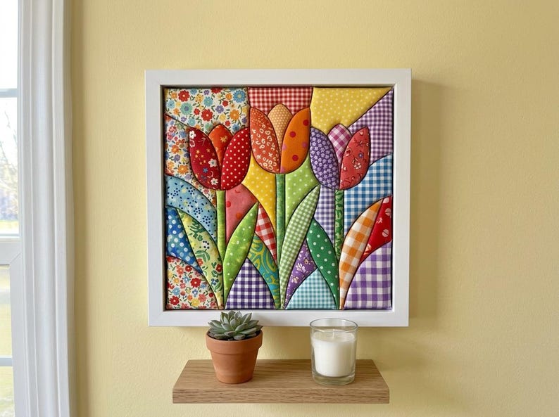 May include: A square wall art piece featuring a fabric-pieced tulip design in a white frame. The tulips are constructed from various colorful patterned fabrics including gingham, floral, and polka dot prints in red, orange, yellow, and purple.