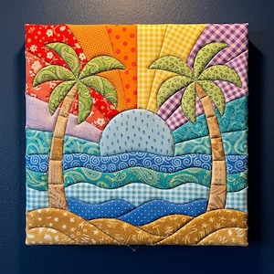 May include: A square fabric wall art piece featuring a quilted tropical scene with two palm trees, a blue sun, and layered waves. The background displays a sunburst pattern in red, orange, yellow, and purple fabrics with various floral and geometric prints.