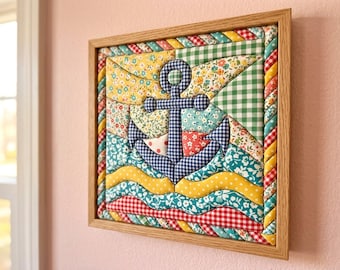 May include: A square fabric wall art piece featuring a central navy and white gingham anchor appliqué. The background consists of quilted fabric sections in floral, polka dot, and gingham patterns in yellow, green, red, and blue, all encased in a light wood frame.