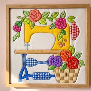 May include: A framed fabric wall art piece featuring a yellow sewing machine appliqué on a white background. The machine is decorated with colorful fabric roses, green leaves, and a woven basket. The base has blue and white checkered patterns.