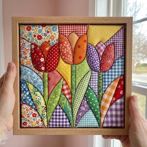 May include: A square fabric wall art piece featuring a quilted tulip design in a light wood frame. The artwork displays three stylized tulips made from various colorful patterned fabrics, including floral, gingham, polka dot, and plaid prints.