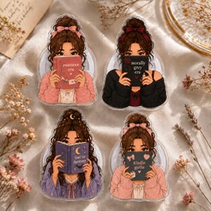 May include: Four acrylic pins featuring illustrated figures with brown hair in buns, each holding a book. The books are titled romance era, morally grey era, lost in fantasy, and kindle girlie. The figures wear sweaters in pink, black, and purple.
