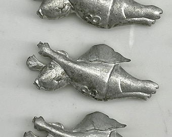 May include: Three silver metal figurines of a creature with wings, possibly a dragon or griffin. Each figurine is in a flying pose with its wings spread out. The figurines are all facing the same direction and are arranged in a row.