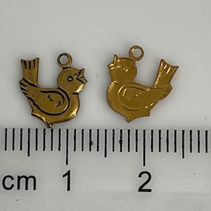 May include: Two gold-colored metal bird charms with a detailed design. The charms are about 1.5 inches long and have a loop at the top for attaching to a necklace or bracelet.