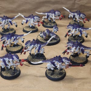 Puede incluir: Colección de figuras en miniatura pintadas de un ejército Tiránido. Las figuras son principalmente blancas y moradas con detalles rojos, montadas sobre bases texturizadas. Los modelos están en poses dinámicas.
