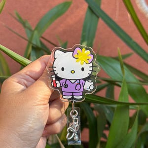 May include: A clear badge reel featuring a cartoon character in a purple medical uniform with a stethoscope. The character has a yellow bow and is holding medical supplies. A silver stethoscope charm hangs below.