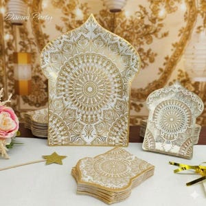 May include: White and gold decorative paper plates and napkins with an intricate mandala design. The plates are shaped like an arch. The text "Damai Party" is visible in the upper left corner.