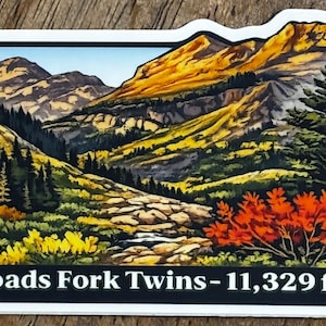May include: A rectangular sticker featuring a mountain landscape with the text "Broads Fork Twins - 11,329 ft". The image depicts a valley with a stream, trees, and mountains in shades of green, yellow, and orange.