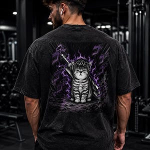 Könnte beinhalten: Ein anthrazitfarbenes T-Shirt in Acid-Wash-Optik mit einem Rückenaufdruck, der eine getigerte Katze mit stacheligem Haar zeigt, die vor einem großen Schwert sitzt. Die Katze ist von violetter Energie und schwebenden japanischen Katakana-Zeichen umgeben.
