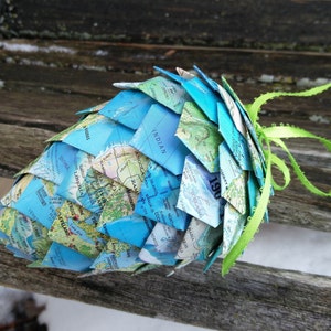 May include: A blue and green paper pinecone ornament made from a world map. The pinecone is decorated with a green ribbon.