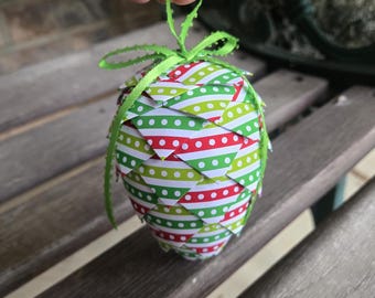 Könnte beinhalten: Handgefertigter Weihnachtsbaumschmuck aus Papier in Form eines Tannenzapfens. Der Schmuck ist mit rot-weiß gestreiftem Papier, grün-weiß gepunktetem Papier und grünem Band verziert. Der Schmuck ist etwa 10 cm hoch.