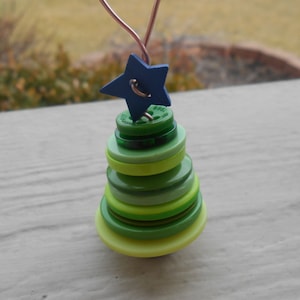 Könnte beinhalten: Ein grüner und gelber Knopf-Weihnachtsbaumschmuck mit einem blauen Stern oben drauf.