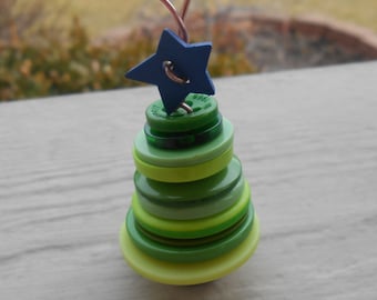Può includere: Un ornamento per albero di Natale a forma di albero di Natale in bottoni verdi e gialli con una stella blu in cima.