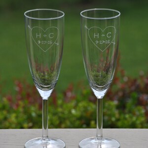 May include: Two clear glass champagne flutes with etched hearts and the initials H+C and the date 9-17-16. The flutes are on a wooden surface.