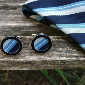 Peut inclure: Deux boutons de manchette argentés avec un motif rayé bleu et blanc à l'intérieur de la face du bouton de manchette.