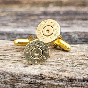 May include: A pair of gold cufflinks made from repurposed .45 Auto Winchester bullet casings. The cufflinks feature the original markings of the bullet casings, including the caliber and manufacturer.