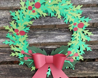 May include: A paper Christmas wreath with green leaves and red berries, decorated with a large red bow.