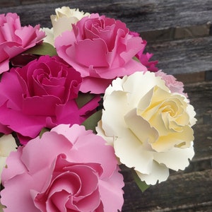 May include: A bouquet of paper flowers in a glass vase. The flowers are pink, white, and yellow. The flowers are arranged in a vase on a wooden surface.