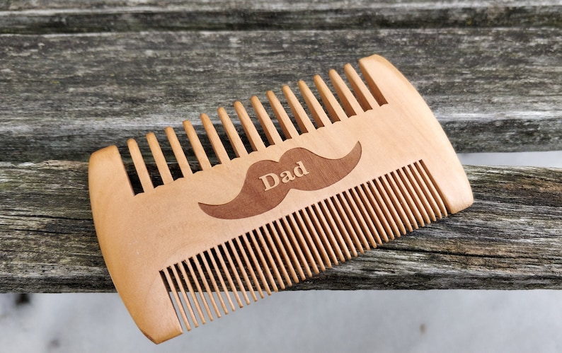 Peut inclure: Un peigne en bois avec un motif de moustache et le mot "Papa" grav&eacute; dessus.