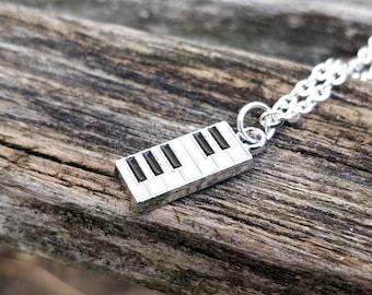 Puede incluir: Collar de plata con un dije de tecla de piano. El dije es de plata con teclas negras.