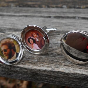 May include: A pair of silver cufflinks with a hinged locket design. One cufflink features a photo of a couple, while the other cufflink is closed and reflective.