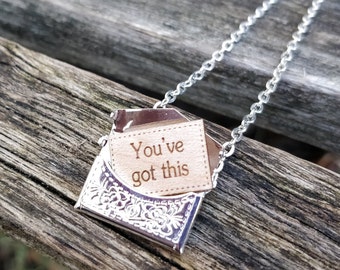 May include: A silver necklace with a small silver envelope charm. The envelope has a wooden insert with the words "You've got this" engraved on it.