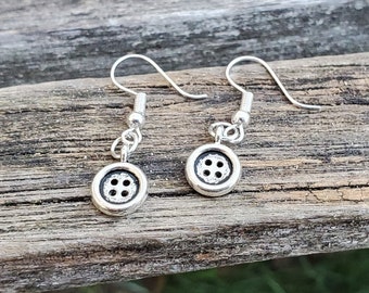 May include: A pair of silver earrings with button-shaped charms. Each charm has a silver button with four holes in the center.