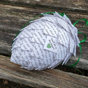 Pode incluir: Uma esfera de papel branco com fita verde, feita de notas de papel dobradas com mensagens escritas &agrave; m&atilde;o. A esfera &eacute; decorada com um pequeno cora&ccedil;&atilde;o verde e o texto "You'll be in my heart" escrito em uma etiqueta branca.