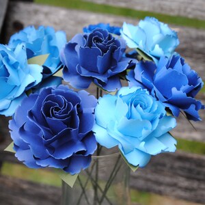 May include: A bouquet of blue and light blue paper flowers. The flowers are arranged in a clear glass vase.