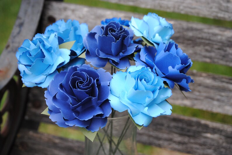 May include: A bouquet of blue and light blue paper flowers. The flowers are arranged in a clear glass vase.
