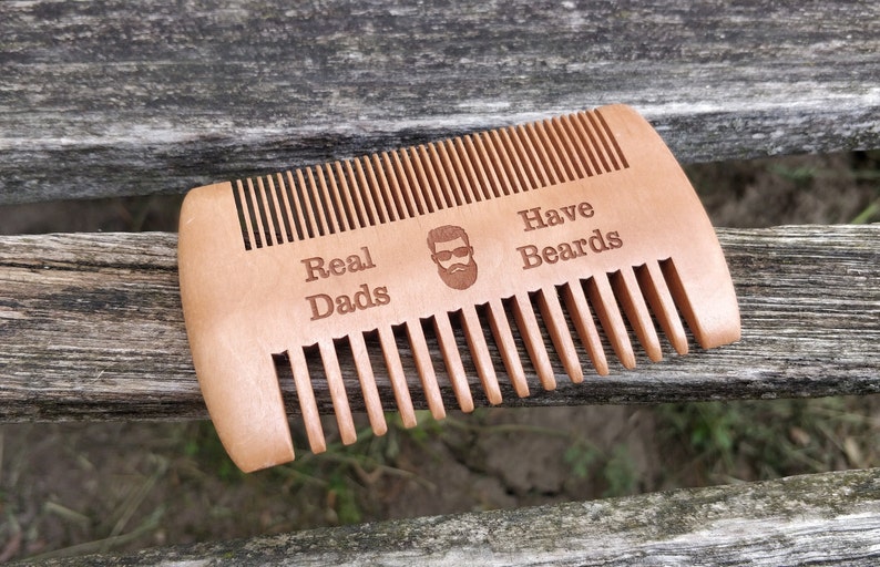 Peut inclure: Un peigne en bois avec le texte "Real Dads Have Beards" et une image de dessin anim&eacute; d'un homme avec une barbe et des lunettes de soleil.