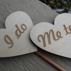 May include: Two wooden heart-shaped signs with the text "I do" and "Me too" on them. The signs are attached to wooden sticks.