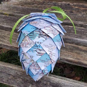 May include: A blue and green paper pinecone ornament made from a map of Jamaica. The pinecone is made of folded paper and has a green ribbon attached to the top.