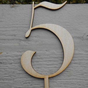May include: A wooden number five with a decorative, cursive font. The number is light brown and has a small, thin stem at the bottom.