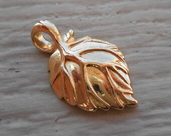 May include: A gold-colored leaf charm pendant with a detailed design. The pendant has a loop at the top for attaching to a chain or cord.