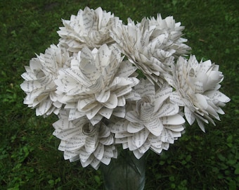 Puede incluir: Un ramo de flores de papel blanco hechas con páginas de libros. Las flores están dispuestas en un jarrón y tienen un aspecto vintage y rústico.