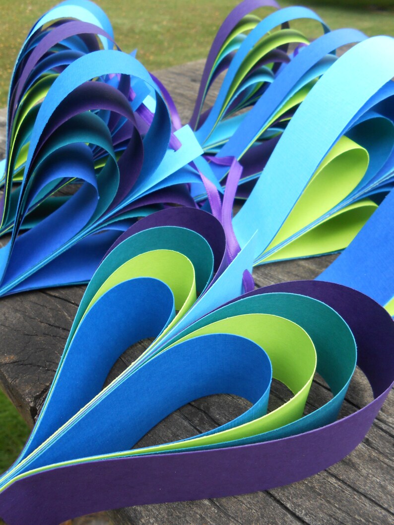 Pu&ograve; includere: Un cuore di carta artigianale realizzato con strisce di carta blu, verde e viola. Il cuore &egrave; piegato in un motivo a strati, creando un effetto tridimensionale.